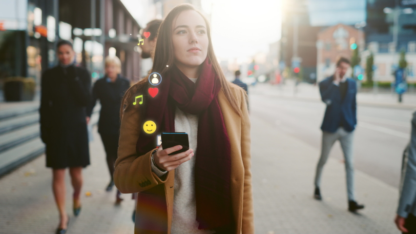 Beautiful Happy Young Woman Uses Smartphone with Animated Social Media Icons Flying Away, Walks on Crowded City Streets. Social Network Concept, Likes, Emoticons, e-business.  Royalty-Free Stock Footage #1058828548