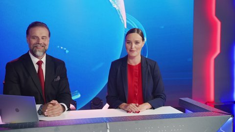 Live News Studio with Beautiful Female and Handsome Man Anchors Start Reporting. TV Broadcasting Channel with Presenters Talking. Inside Mock-up Television Newsroom Set. Zoom in Descending Shot
