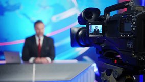 Professional TV Camera Standing in Live News Studio with Anchor seen in Small Display. Unfocused TV Broadcasting Channel with Presenter, Newscaster Talking. Mock-up Television Channel Newsroom Set