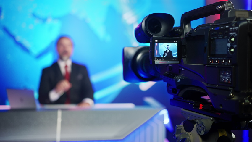 Professional TV Camera Standing in Live News Studio with Anchor seen in Small Display. Unfocused TV Broadcasting Channel with Presenter, Newscaster Talking. Mock-up Television Channel Newsroom Set Royalty-Free Stock Footage #1058828704