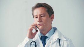 serious doctor in white coat talking on smartphone on grey