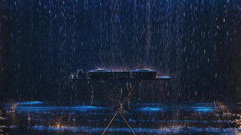 Wet from the rain Pro dj controller. The DJ console deejay mixing desk and professional headphones against the background of a dark studio under drops of rain. Slow motion.