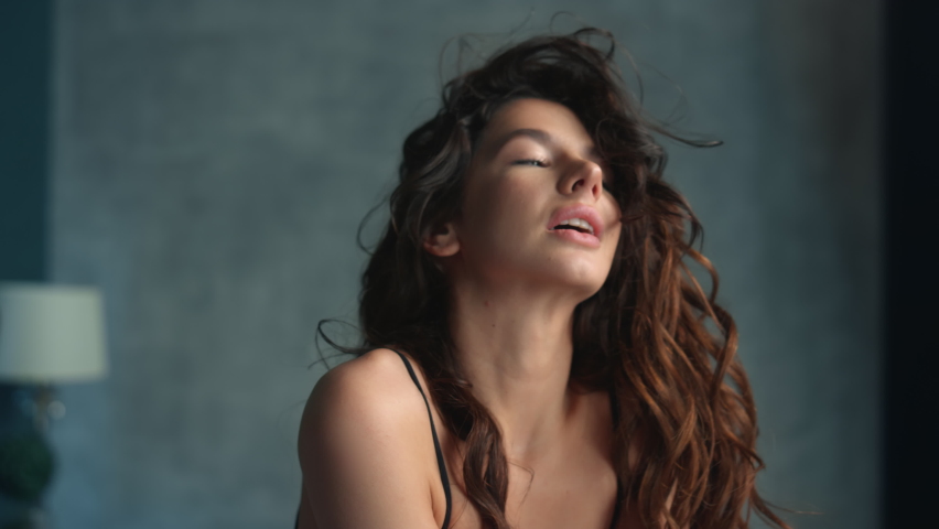 Portrait of hot woman touching hair in bedroom in slow motion. Closeup sensual girl relaxing at home. Young fashion model smiling camera indoors.