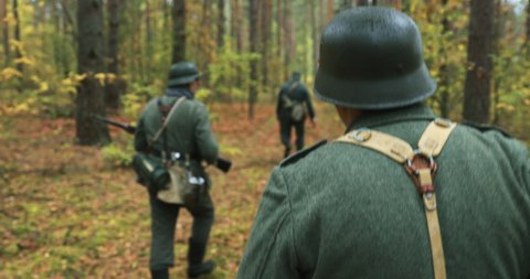 Historical Re-enactment. Re-enactors Dressed German Wehrmacht Infantry Soldiers In World War II Marching Along Forest In Autumn Day. Group of Soldiers Marching In Forest.