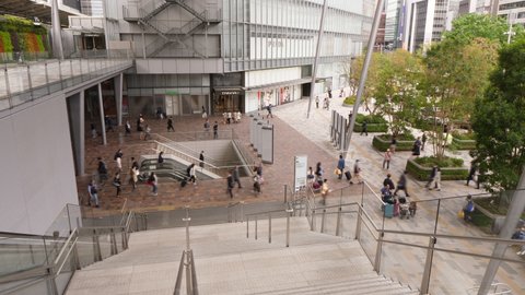 TOKYO - APRIL 06, 2018: Commuters walk at Tokyo Station Yaesu entrance, time lapse shot at day. Modern design of urban space, green square seen on right, large department store in building