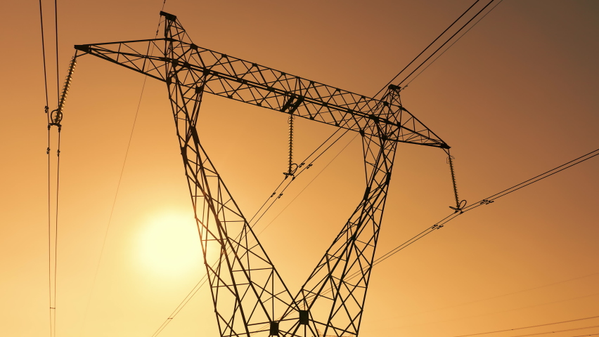 Transmission tower supporting an overhead high voltage power line - silhouette at sunset. The pylon carries wires that transport electric power from generating stations to electrical substations. | Shutterstock HD Video #1058841562