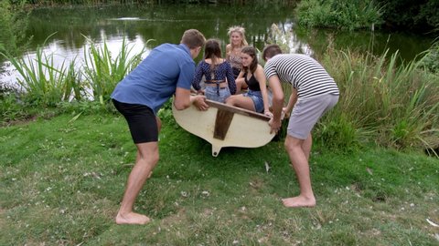 Friends pushing rowboat into lake, Dinton, Wiltshire, United Kingdom