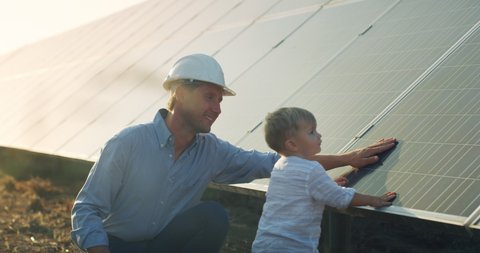 An young engineer father is explaining to his little son an operation and performance of photovoltaic solar panels at sunset. Concept:renewable energy, technology, electricity, green,future, family