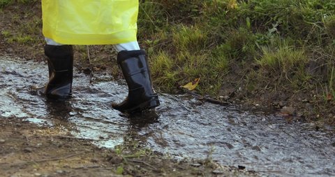 woman in a yellow raincoat and rubber boots jumping through puddles