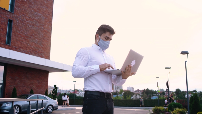 Businessman in medical masks is sitting on the terrace of a cafe and working on a laptop, view through the glass, protection from the virus, working during the pandemic.