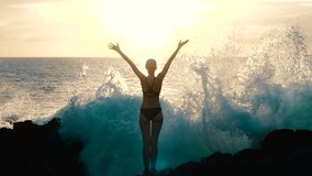 Silhouette woman at sunset raising arms in air and observing ocean waves crashing on rocks and spraying. Concept of explosion of emotions, joy, happiness in life. Traveling around world, slow motion.  - Powered by Shutterstock - Get 15% off with code: PIKWIZARD15