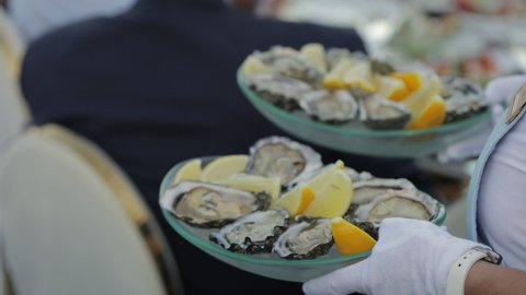 The waiter is carrying a dish with oysters, lemon and orange slices. Preparing for the banquet at the event. 