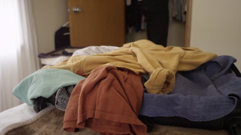 Man throwing clothes from his closet into a suitcase on the bed