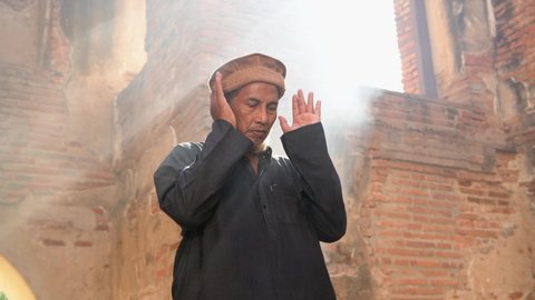 Silhouette of a Muslim man in prayer and the Islamic rituals in a room where sunlight shines through the mosque door.With light and smoke in the background