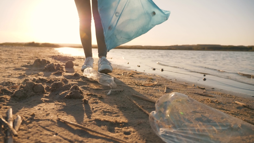 Teamwork cleaning plastic on the beach. Volunteers collect trash in a trash bag. Plastic pollution and environmental problem concept. Voluntary cleaning of nature from plastic. Greening the planet | Shutterstock HD Video #1058858656