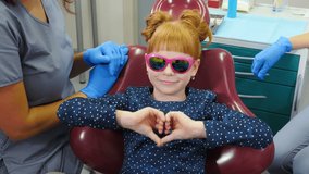 Smiling confident child at dentist office. happy little girl wearing sun glasses sitting in dental chair showing thumbs up after dental check up. Pediatric dentistry. 4 k video
