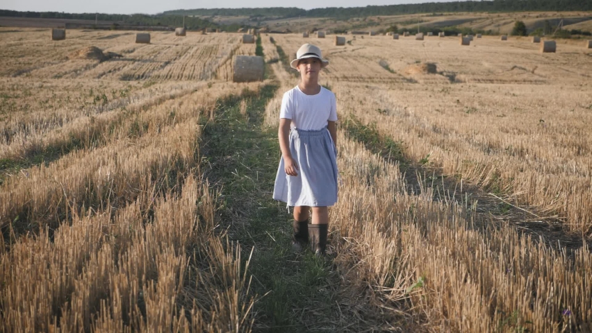 Pretty girl in blue dress walks in a field with haystacks.