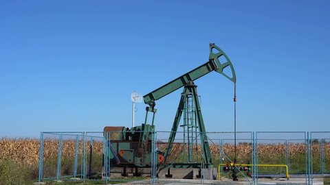 Pump Jack Extracting Crude Oil from a Oil Well. Fossil Fuel Energy. Oil Industry Equipment. Petroleum Industry Pump Jack Against Blue Sky.