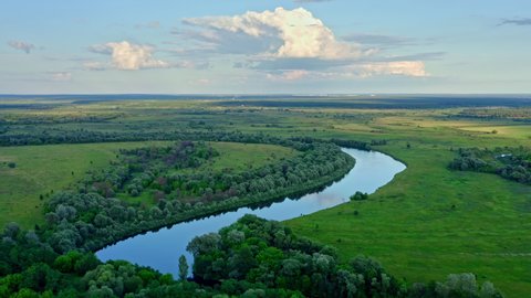 Aerial cinematic: drone flies  above a beautiful summer  landscape with a river while sunset. Aerial view from drone flies over a amazing landscape in spring. Bird view to the long river