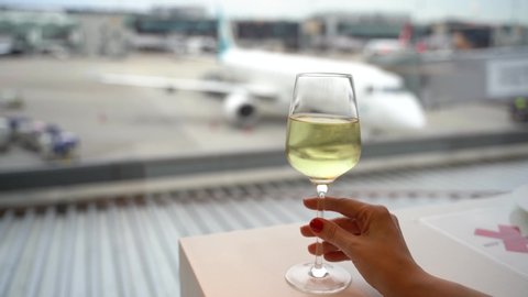 Female hand holding a glass of wine near window in an airport with a view to a white airplane