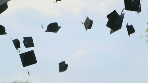 Close up in slow motion of university high school graduates throwing their square academic tudor bonnet cap into the air graduation ceremony. Students Celebration of a MBA bachelor and master degree