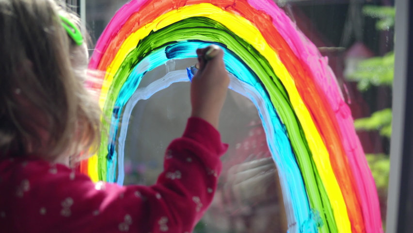 Girl draws a rainbow with paints on the window