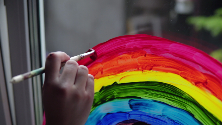 Painting a rainbow with paints on a window close-up