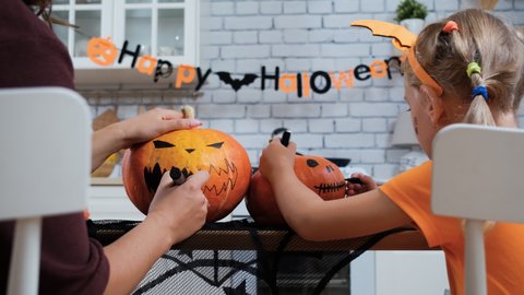 Closeup of Woman with Little Daughter Paint Pumpkins for Halloween while Sitting at the Table in the Kitchen. Preparing Decorations for Halloween Party at Home