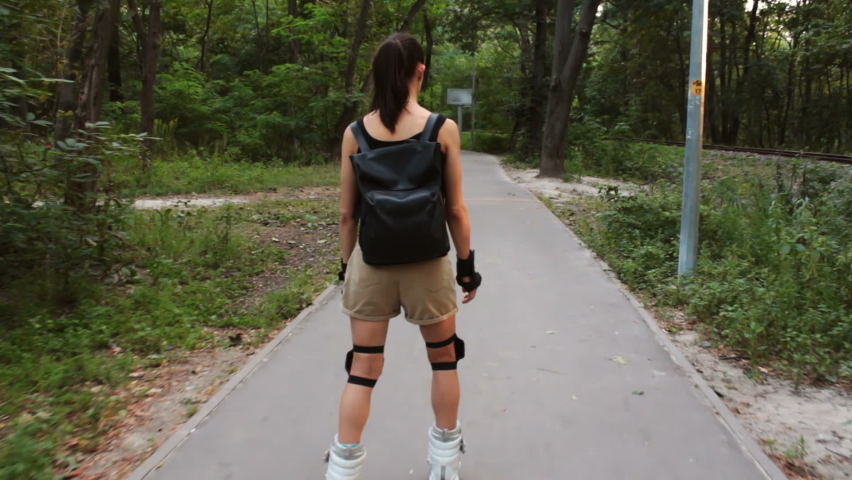 Young happy female enjoy roller skating in the summer park. Young attractive female is rollerblading in the park.