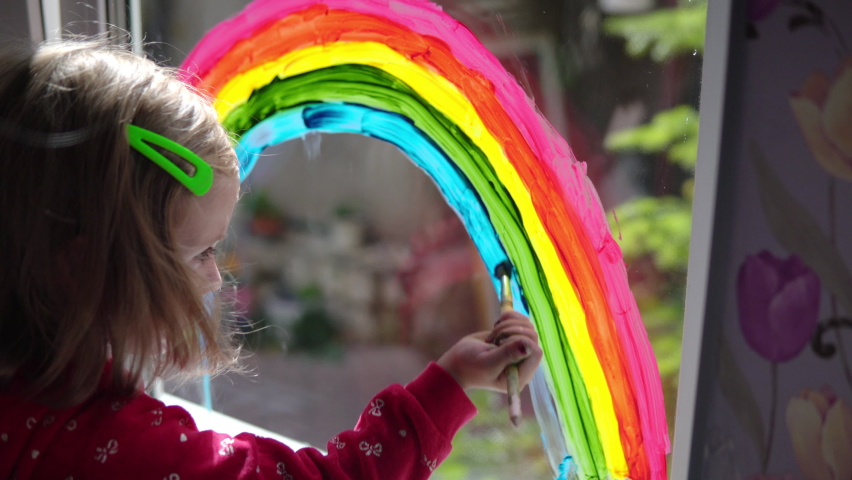 Girl draws a rainbow with paints on the window
