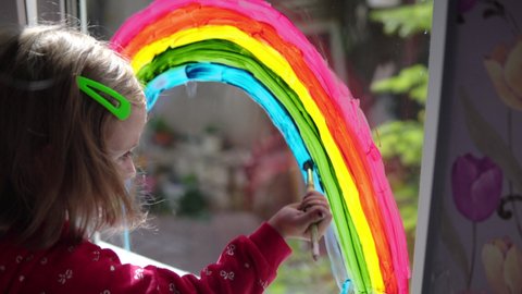 Girl draws a rainbow with paints on the window