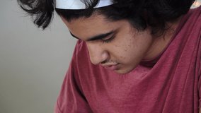 Close up of teen boy of Persian ethnicity doing remote school in times of Covid-19, taking math notes from a virtual lesson on his laptop. Matching medium shot available.