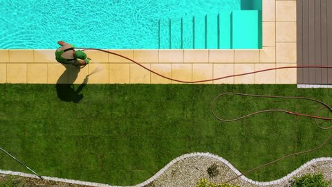 Aerial View Of Male Lawn Installer Watering Newly Placed Natural Turf And Cleaning Edge Tiles Of Outdoor Swimming Pool.