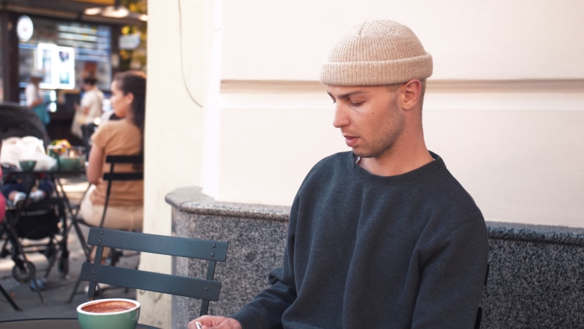A portrait of a young caucasian man takes off a medical mask. A man sits in a cafe outside