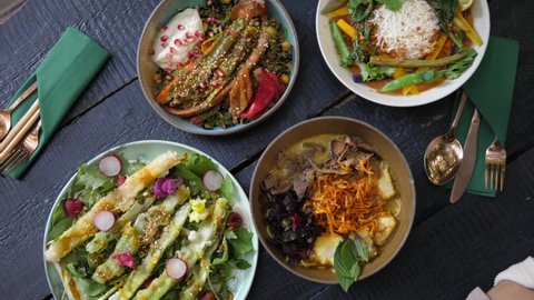 Top view of people eating their healthy vegan meals with chopsticks. Bowls full of colorful vegetables served on black chunky wooden table