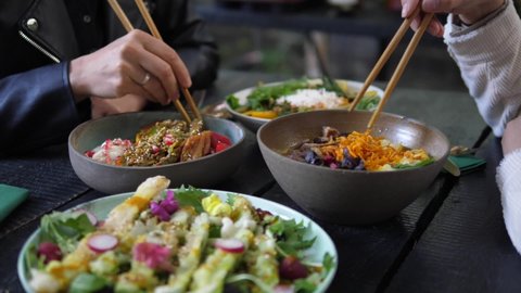 Healthy Asian vegan lunch served in rustic cafe. Two people eating their healthy vegan meals with chopsticks
