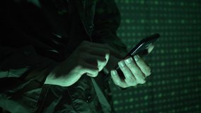 Hacker using a mobile phone to hack the system. He is standing in the dark with a matrix-like background. - Powered by Shutterstock - Get 15% off with code: PIKWIZARD15