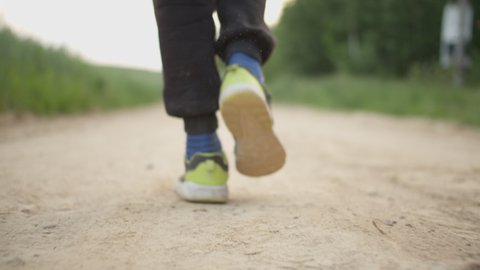close-up of a boy's feet walking along a country road in dirty clothes