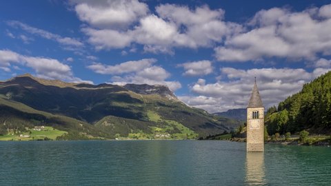 The top of the old bell tower of Curon (Graun) emerges from the waters of Lake Resia, against a dramatic sky, South Tyrol, Italy. Time lapse motion