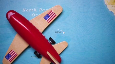 A red plane with a flag of US attached to its wings is crossing the map of HAWAII, USA.