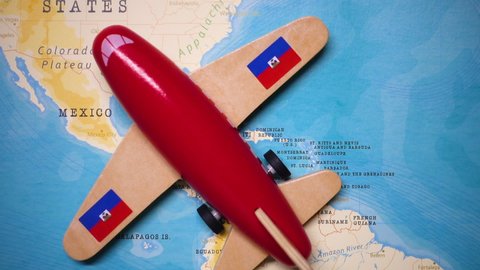 A red plane with a flag of Haiti attached to its wings is crossing the map of Haiti.