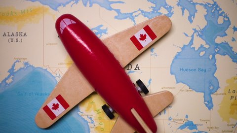 A red plane with a flag of Canada attached to its wings is crossing the map of Canada.