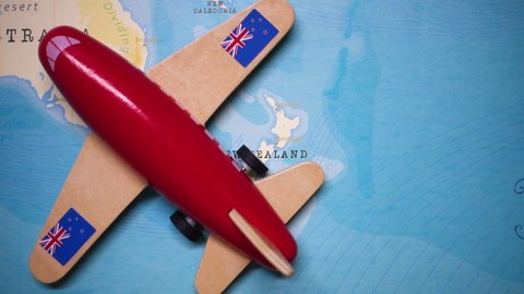 A red plane with a flag of New Zealand attached to its wings is crossing the map of New Zealand.