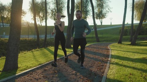 At sunlight man and woman running in park together jogging at outdoor workout sportswear active young workout sport runner fitness cardio summer slow motion