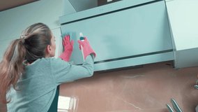 Beautiful young blonde girl wipes the kitchen hood with cleaning agent. Professional cleaner. Hands in pink rubber gloves.