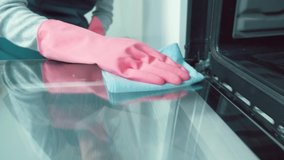 The girl professional cleaner wipes the door in the kitchen with a rag inside the oven. Girl in pink rubber gloves.