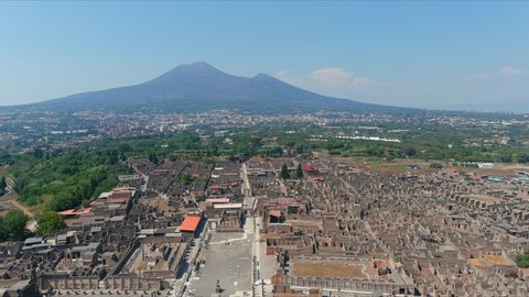 Aerial view of ruins of Pompeii, ancient Roman city destroyed by volcanic eruption of volcano Mount Vesuvius, cone of Mount Vesuvius in background, clear blue sky - Naples, Campania, Italy, Europe