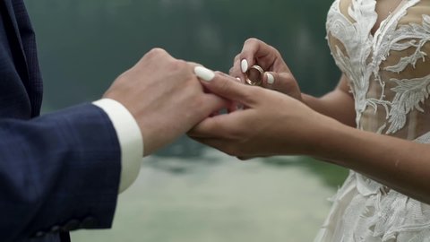 Wedding ceremony on the lake in mountains. Bride puts the ring on groom’s finger. Wedding symbols and traditions. Newlyweds’ hands close up. Hallstatt, Austria