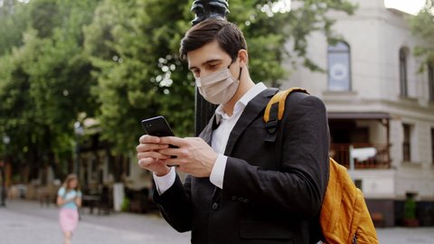 Businessman with a protective mask in quarantine of Covid-19 in the middle of the street typing something on the phone concentrated. Shot on ARRI Alexa Mini