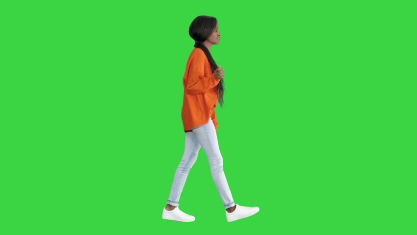 Smiling African American woman dressed in bright sweater and jeans walking touching her hair on a Green Screen, Chroma Key.